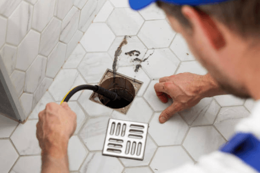 Plumber unclogging blocked shower drain with hydro jetting at home bathroom sewer cleaning service