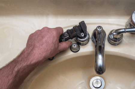 Image of hand using wrench to adjust sink handle - plumbing